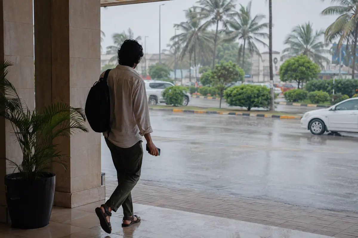 مسافر يغادر فندقًا في صلالة خلال المطر وهو يحمل هاتفه