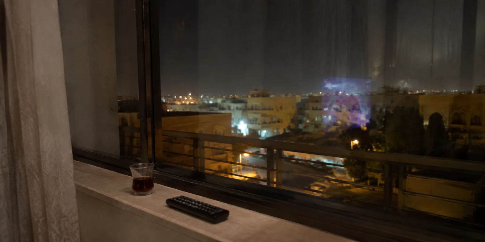منظر ليلي من نافذة شقة في الرياض مع جهاز تحكم وكأس شاي