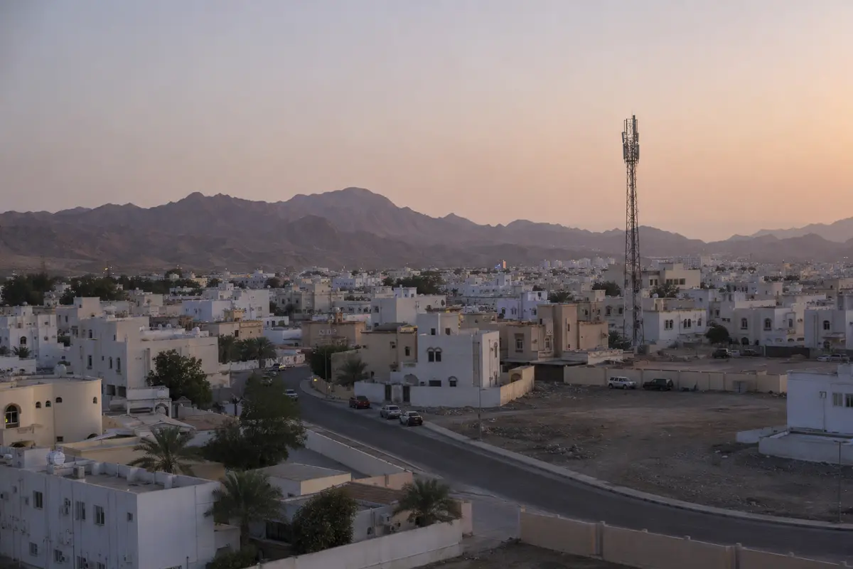 برج اتصالات يرتفع بين أحياء مسقط والجبال وقت الغروب