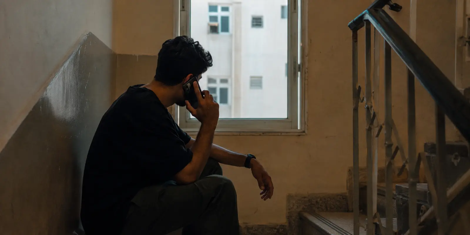 رجل يجلس في درج مبنى ويحاول متابعة مكالمة هاتفية