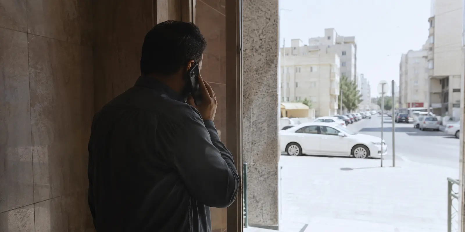 رجل يتوقف عند باب مبنى في الكويت أثناء مكالمة هاتفية