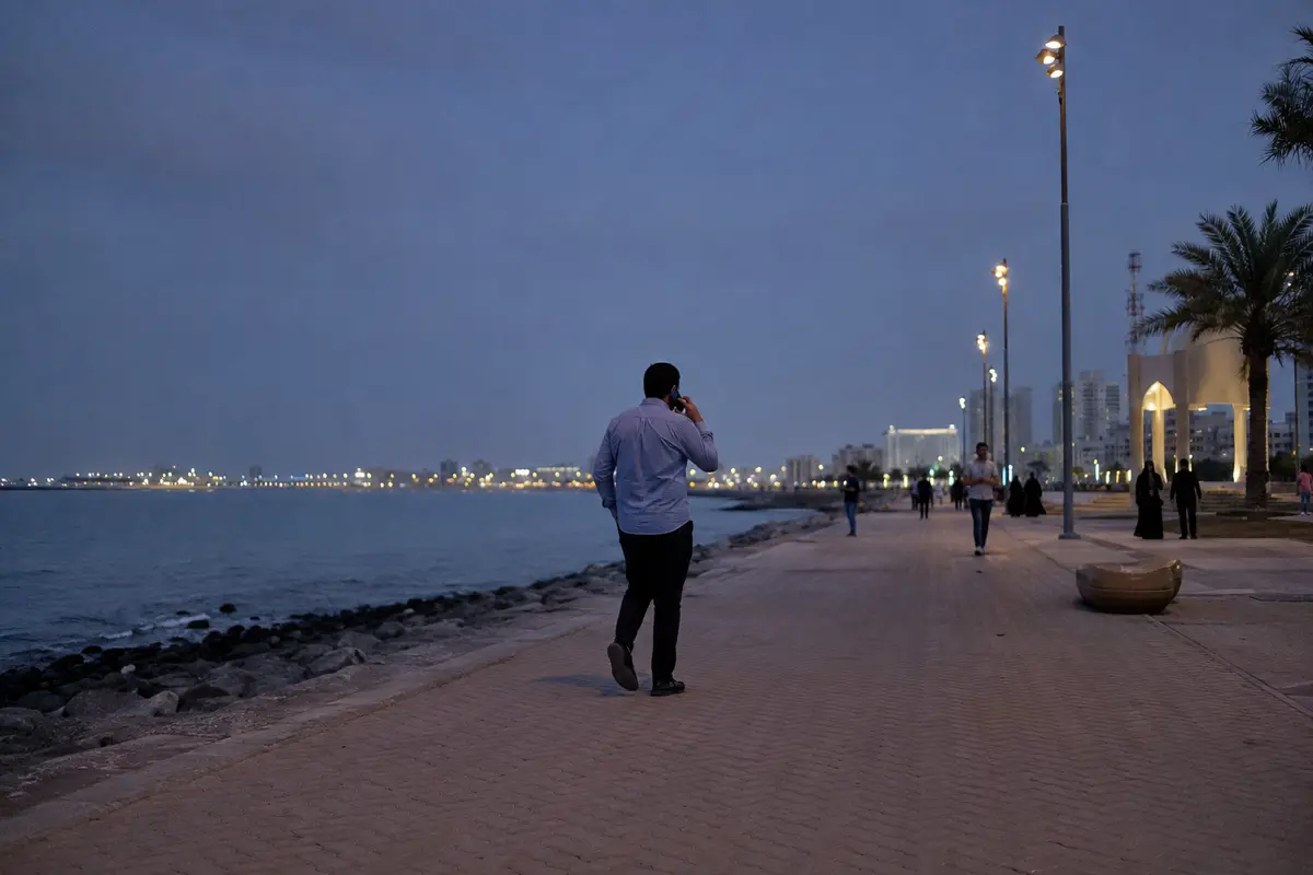 شخص يواصل مكالمته وهو يمشي على الواجهة البحرية في الكويت مساءً