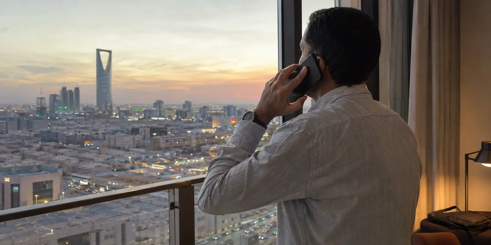 مسافر يجري مكالمة هاتفية أمام أفق الرياض عند الغروب