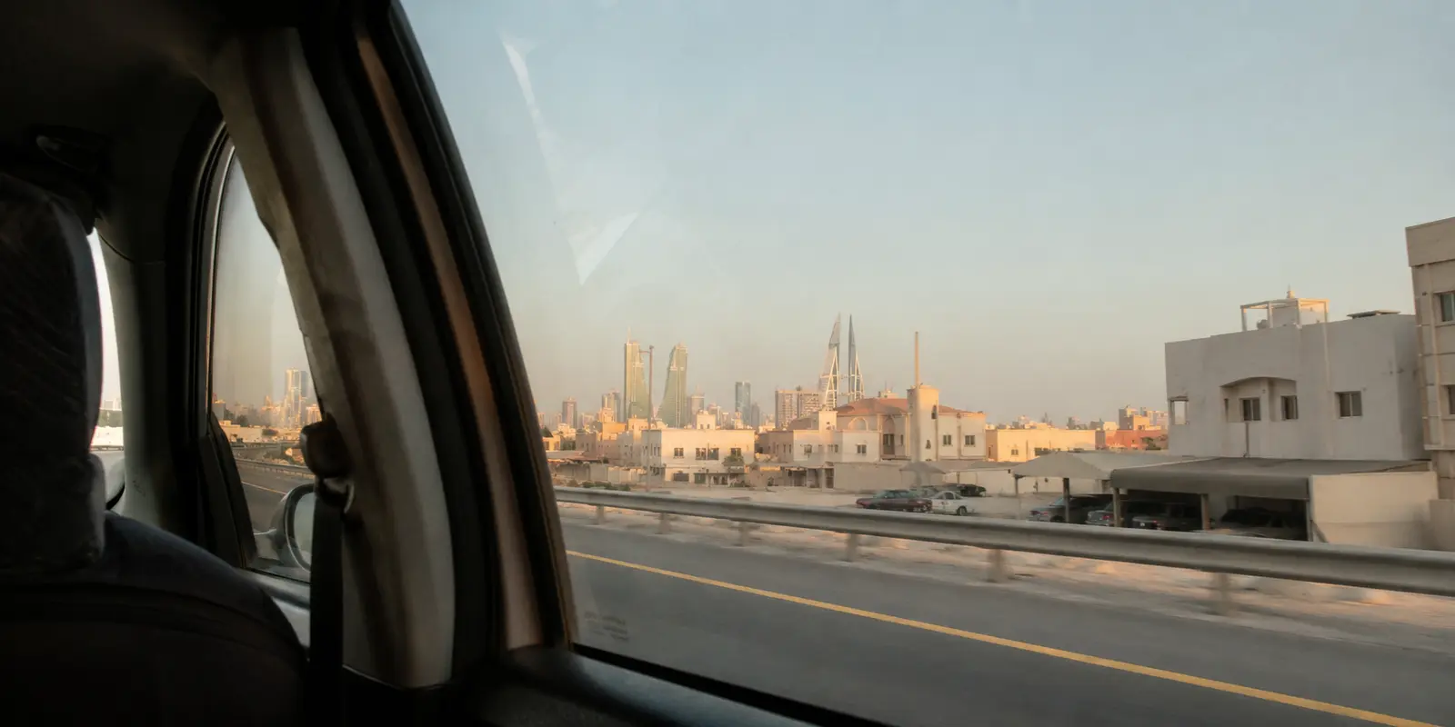 منظر المنامة من نافذة سيارة تسير على طريق المدينة عند الغروب