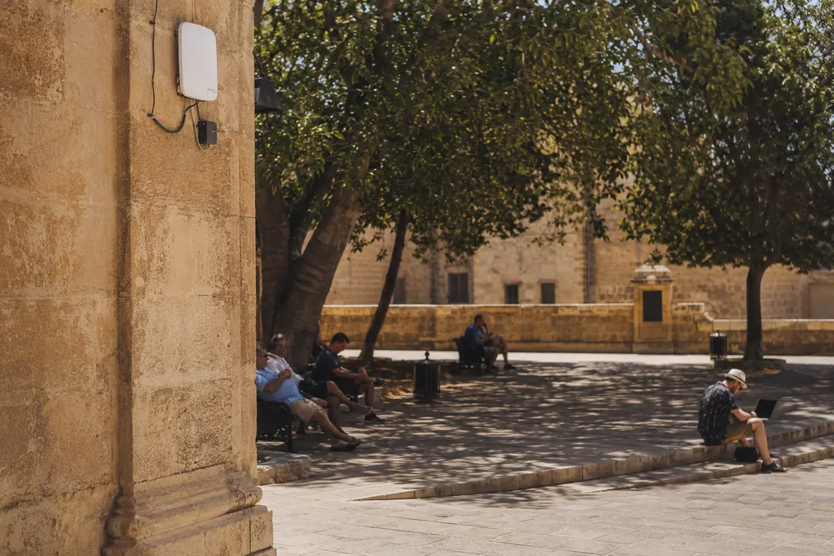 People using public Wi-Fi in a shaded stone square in Malta