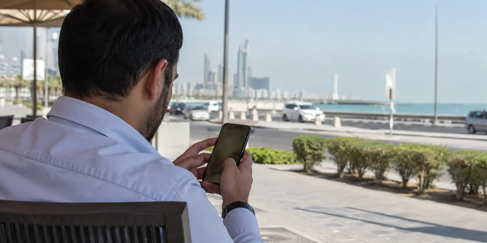 رجل يستخدم هاتفه قرب الواجهة البحرية في مدينة الكويت