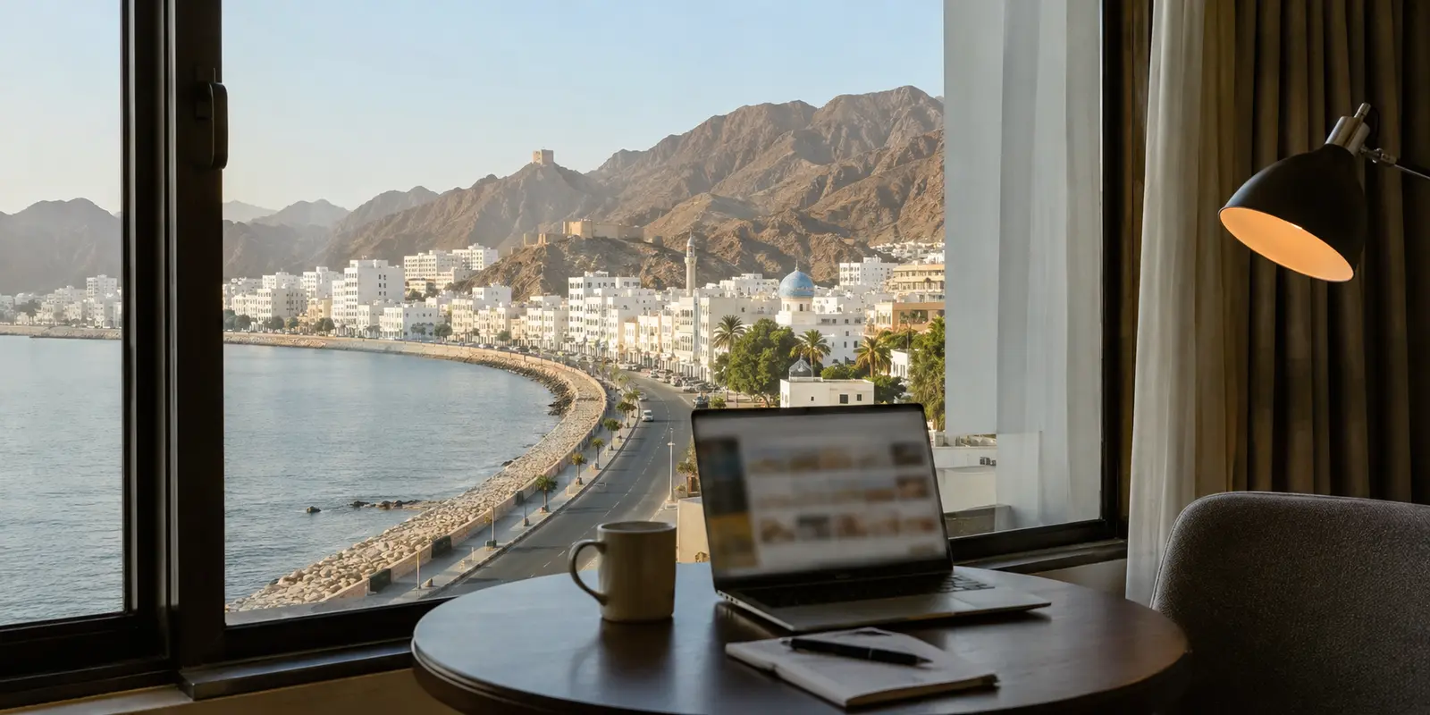 منظر ساحلي لمدينة عُمانية من غرفة مسافر يعمل على حاسوبه