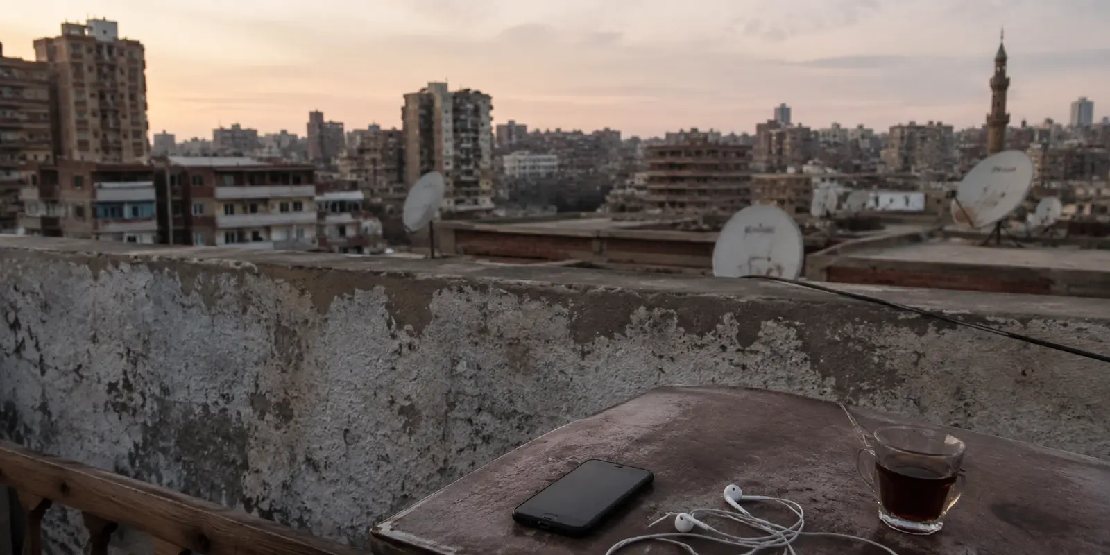 هاتف وسماعات على سطح منزل يطل على أحياء القاهرة عند الغروب