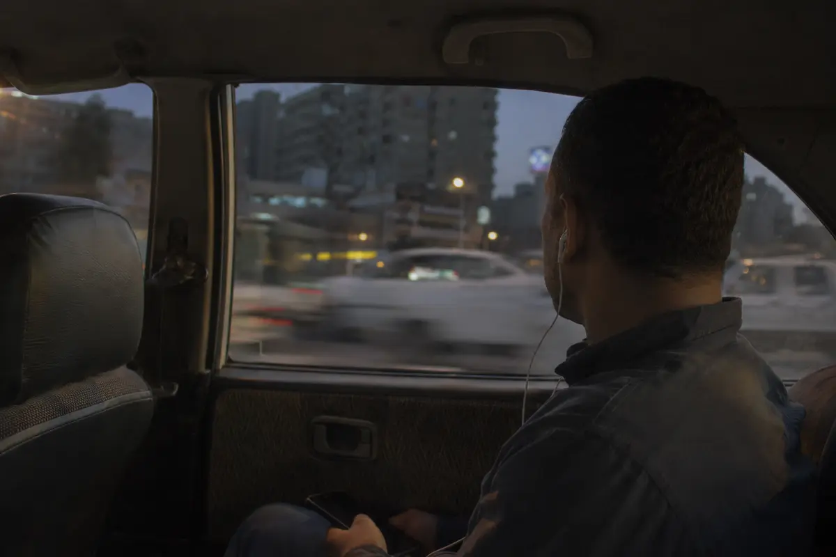 راكب يستخدم سماعات هاتف داخل سيارة تتحرك في شوارع القاهرة مساءً