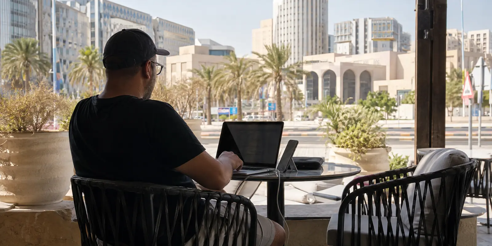 مسافر يعمل عبر نقطة اتصال هاتفه في مقهى خارجي بالدوحة