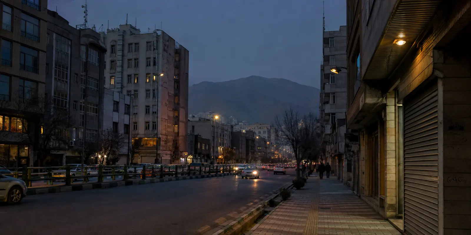 شارع إيراني عند الغسق بين مبانٍ سكنية قديمة وجبال بعيدة