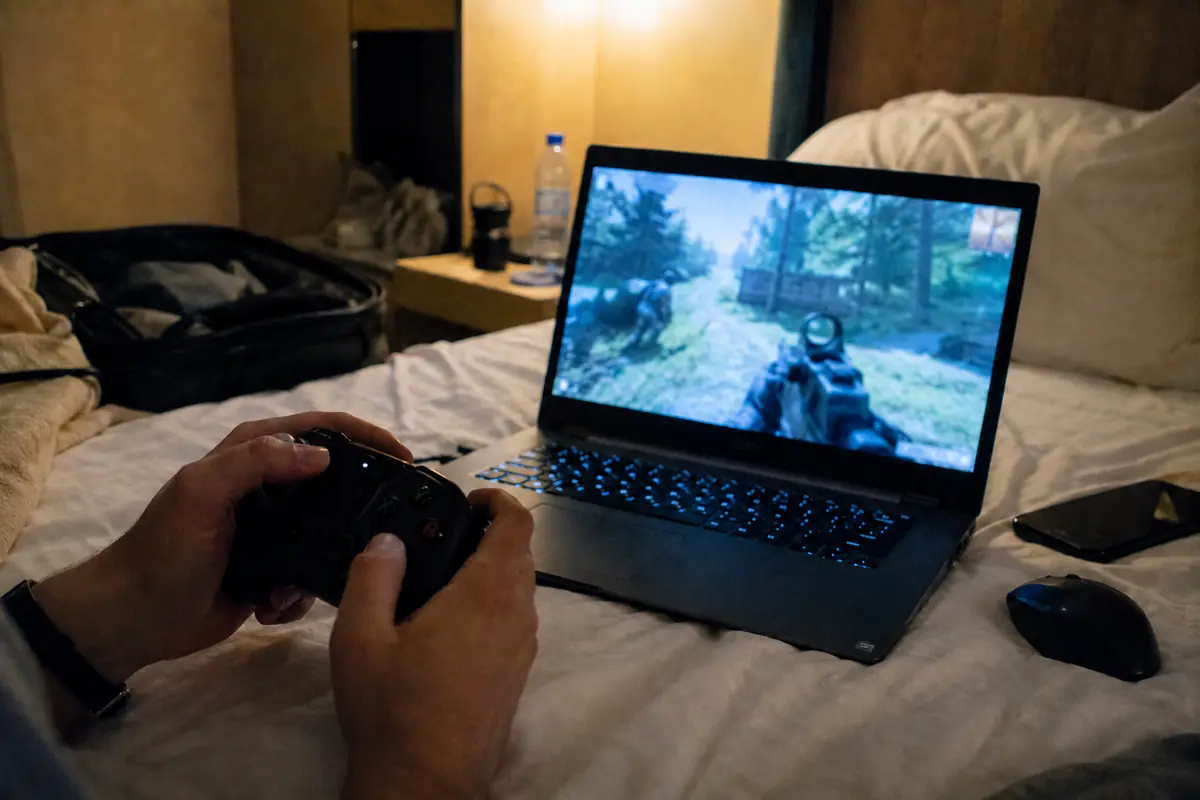 مسافر يلعب مباراة عبر حاسوب محمول على سرير فندق