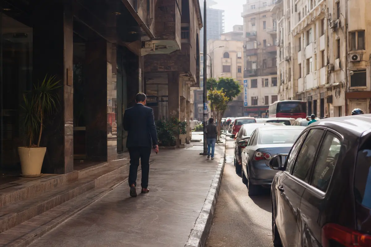 مسافر يغادر مبنى إلى شارع مزدحم في القاهرة وهاتفه بيده