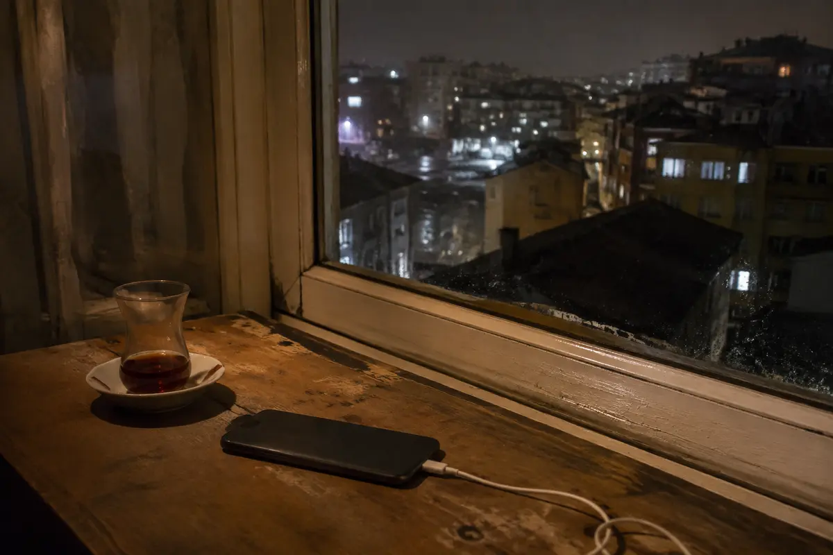 هاتف موضوع بجوار كوب شاي أمام نافذة تطل على إسطنبول ليلًا